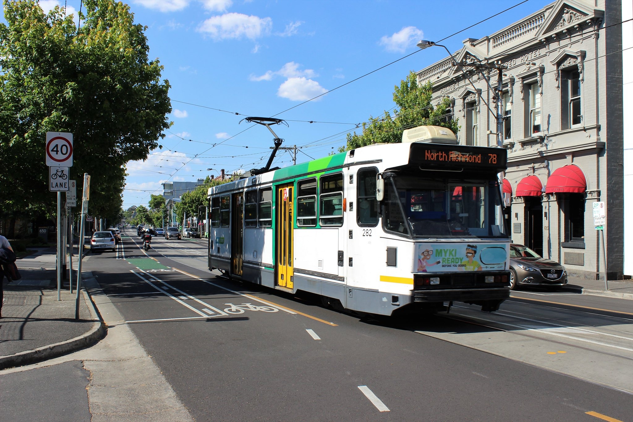 A tram displaying North Richmond travels past a hotel on a tree-lined street